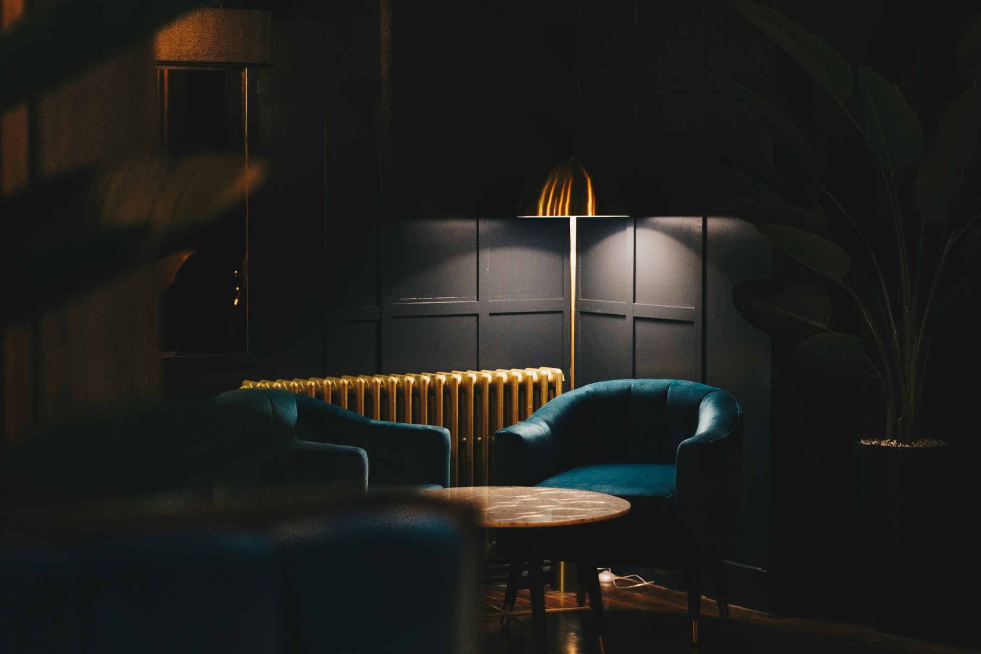 Dimly lit hotel lounge with velvet chairs and a brass floor lamp